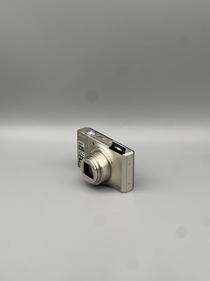 Silver Nikon Coolpix S8000 viewed from the opposite front corner with its lens extended