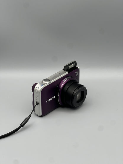 Angled front view of a purple Canon PowerShot SX220 HS with its lens extended and flash raised