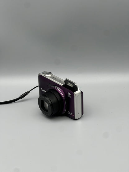 Front and side view of a purple Canon PowerShot SX220 HS with its lens extended and flash raised