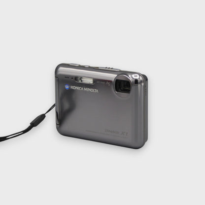 Gray Konica Minolta DiMAGE X1 viewed from a front angle with its lens exposed and wrist strap attached.
