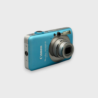 Angled front view of a blue Canon PowerShot SD1200 IS showing its extended lens and silver side panel