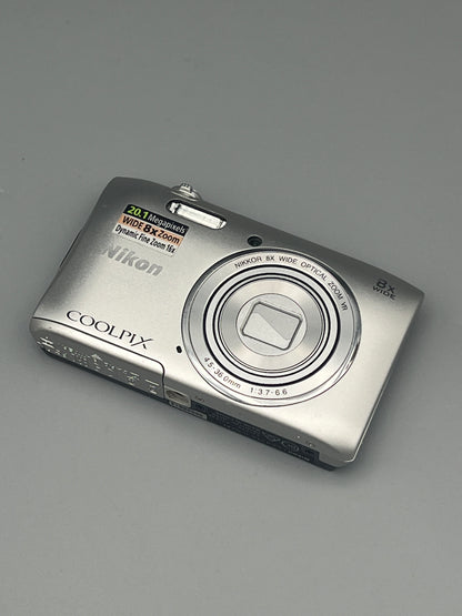 Angled front and underside view of a silver Nikon Coolpix S3600 with its lens closed