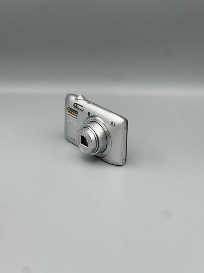 Silver Nikon Coolpix S3600 viewed from the front corner with its lens extended