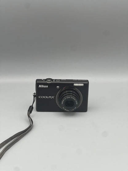 Black Nikon Coolpix S570 front view with its lens extended and wrist strap attached.