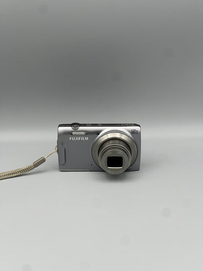 Front view of a silver Fujifilm FinePix T550 digital camera with its lens extended
