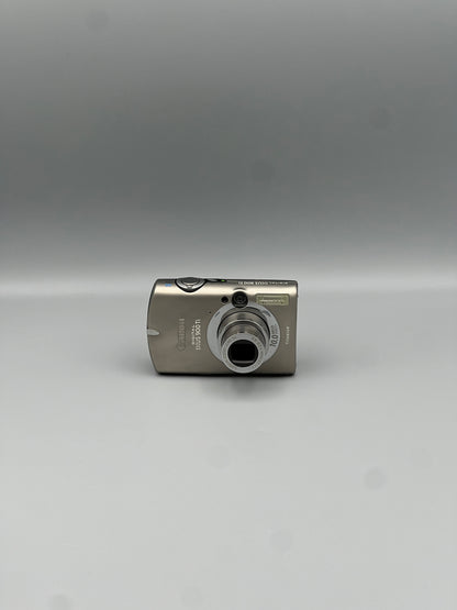 Front view of a silver Canon PowerShot SD900 with its lens extended