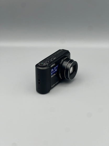 Angled front view of a black Sony Cyber-shot DSC-H70 showing the extended lens and top controls