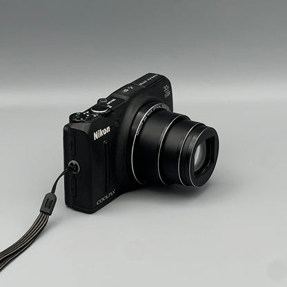 Black Nikon Coolpix S9700 viewed from a front angle showing its extended zoom lens and grip.