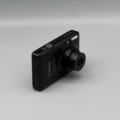 Black Canon PowerShot SD940 IS viewed from a front angle showing its extended lens and side panel.