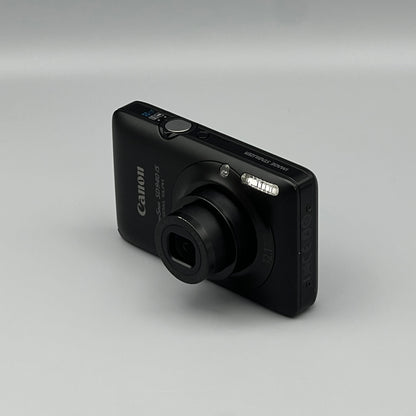 Black Canon PowerShot SD940 IS viewed from above at a front angle with its lens extended.