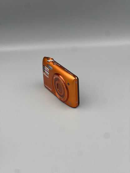 Angled front view of an orange Nikon Coolpix S3500 showing its closed lens and slim side profile
