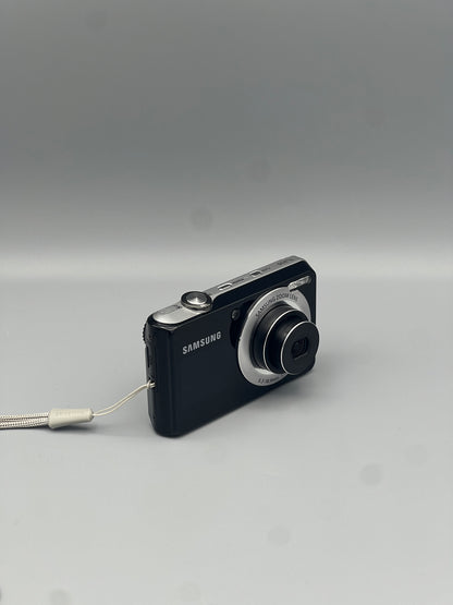 Angled front view of a black Samsung TL205 showing the extended lens and top controls