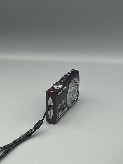 Angled front view of a plum Nikon Coolpix S220 with its lens closed and wrist strap visible