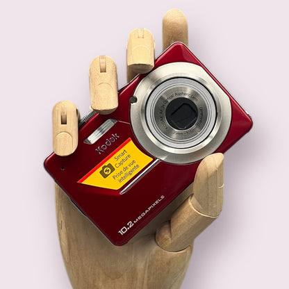 Red Kodak EasyShare M340 held in a wooden display hand with its lens retracted.