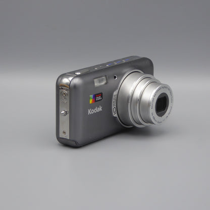 Angled front view of a gray Kodak EasyShare V1003 showing the extended lens and top controls