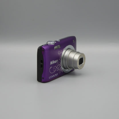 Angled front view of a purple Nikon Coolpix A100 showing the extended lens and top controls