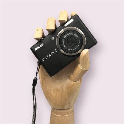 Black Nikon Coolpix S570 held in a wooden display hand with its lens closed.