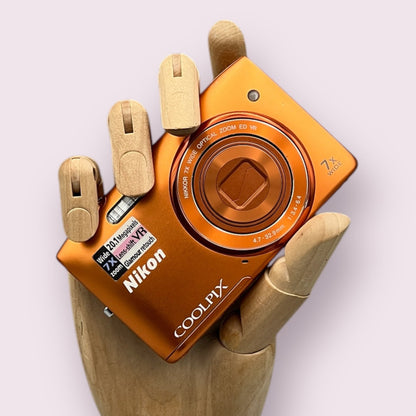 Orange Nikon Coolpix S3500 with its lens closed, held in a wooden display hand