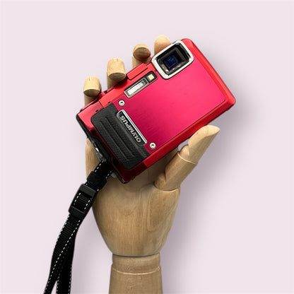 Red Olympus Stylus Tough TG-830 digital camera resting in a wooden hand with a black wrist strap