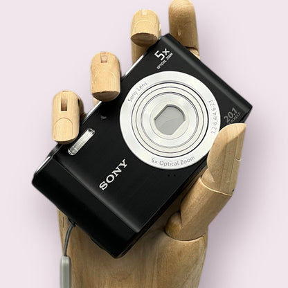 Black Sony Cyber-shot DSC-W800 held in a wooden display hand with its lens closed.