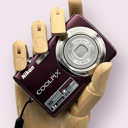 Plum Nikon Coolpix S220 with its lens closed, held in a wooden display hand