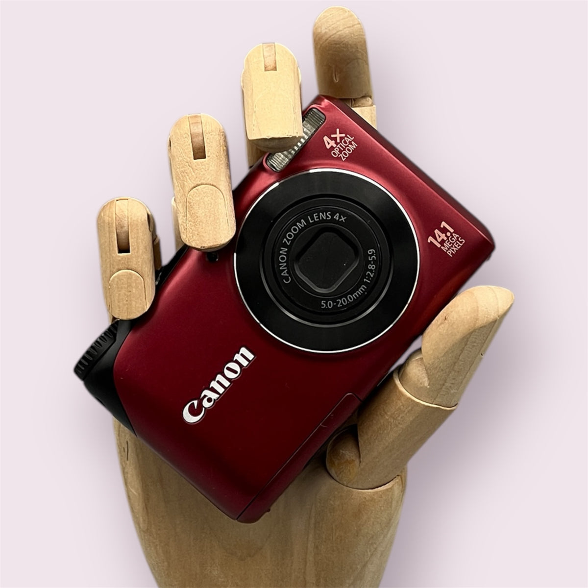 Red Canon PowerShot A2200 with its lens closed, held in a wooden display hand