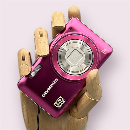 Pink Olympus VG-130 digital camera resting in a wooden hand with the lens closed