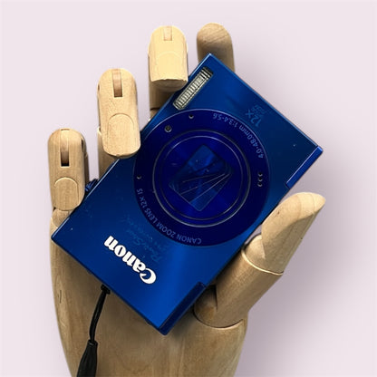 Blue Canon PowerShot ELPH 520 HS held in a wooden display hand with its lens closed.
