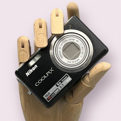Black Nikon Coolpix S560 with its lens closed, held in a wooden display hand