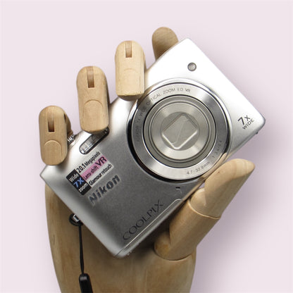 Silver Nikon Coolpix S3500 with its lens closed, held in a wooden display hand