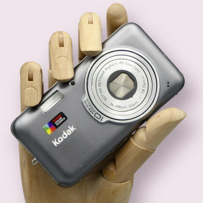 Gray Kodak EasyShare V1003 digital camera resting in a wooden hand with the lens closed