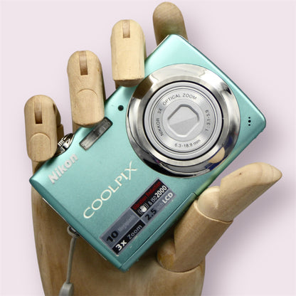 Mint green Nikon Coolpix S220 with its lens closed, held in a wooden display hand