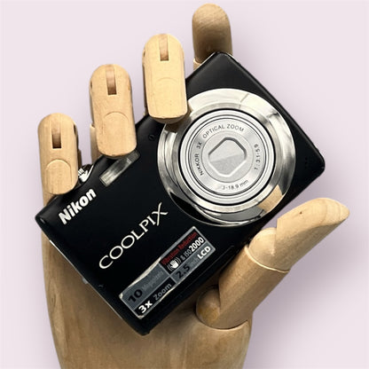 Black Nikon Coolpix S220 with its lens closed, held in a wooden display hand