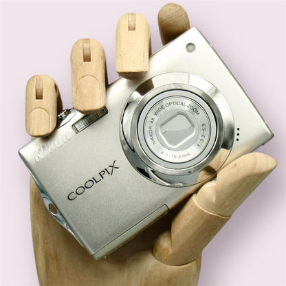 Silver Nikon Coolpix S4000 with its lens closed, held in a wooden display hand
