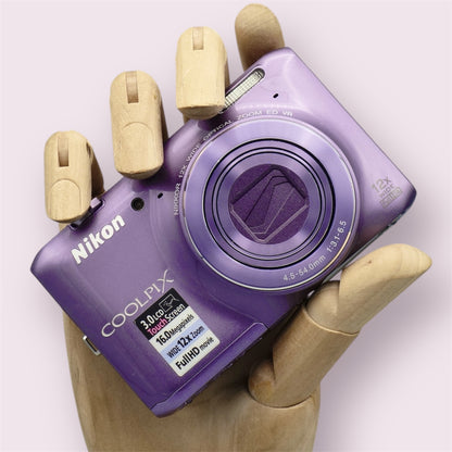 Purple Nikon Coolpix S6400 held in a wooden display hand with its lens closed.