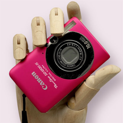 Pink Canon PowerShot SD1200 IS with its lens closed, held in a wooden display hand