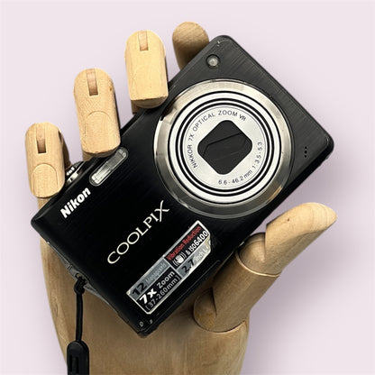 Black Nikon Coolpix S630 digital camera resting in a wooden hand with the lens closed