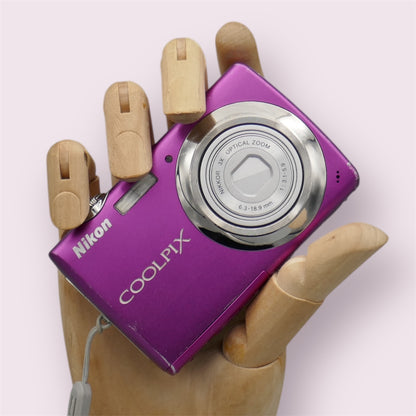 Pink Nikon Coolpix S220 with its lens closed, held in a wooden display hand