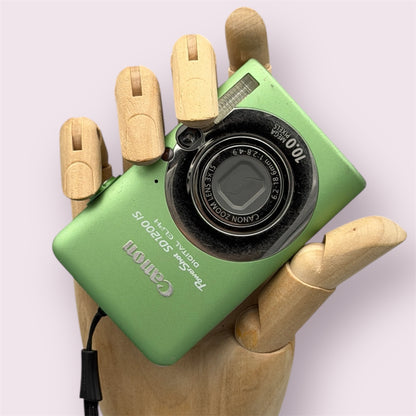 Green Canon PowerShot SD1200 IS with its lens closed, held in a wooden display hand