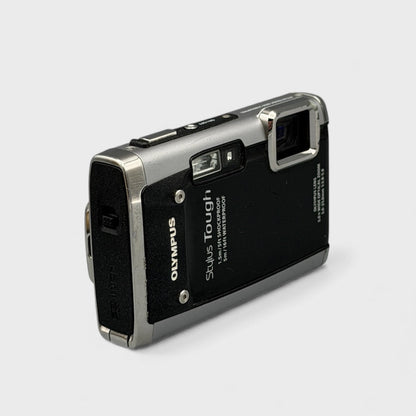 Angled front view of a black and silver Olympus Tough 6020 showing the exposed lens and top controls