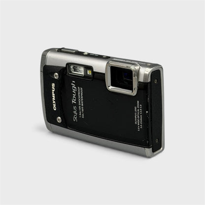 Front and side view of a black and silver Olympus Tough 6020 showing the exposed lens