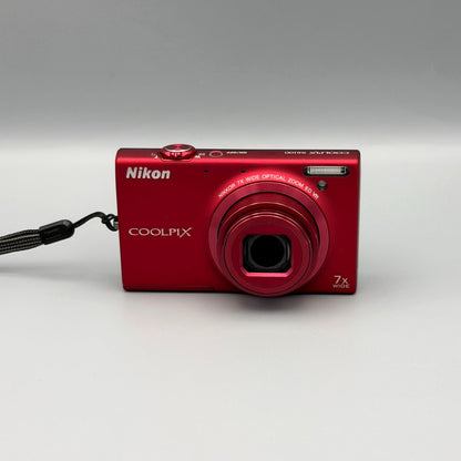 Red Nikon Coolpix S6100 front view with its lens extended and wrist strap attached.
