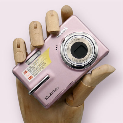 Pink Kodak EasyShare M1073 IS held in a wooden display hand with its lens retracted.