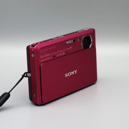 Angled front view of a pink Sony Cyber-shot DSC-TX9 showing the exposed lens and top controls