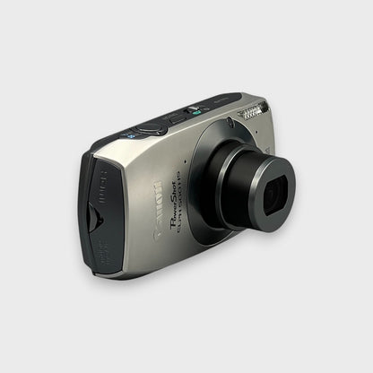 Angled front view of a silver Canon PowerShot ELPH 500 HS showing the extended lens and top controls