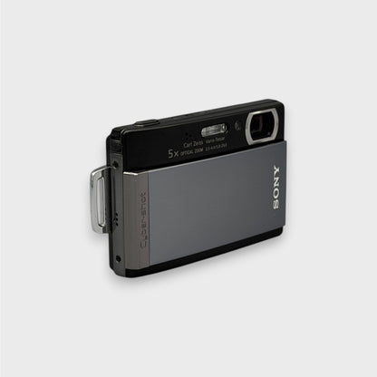 Angled front view of a gray and black Sony Cyber-shot DSC-T300 showing the exposed lens and top controls