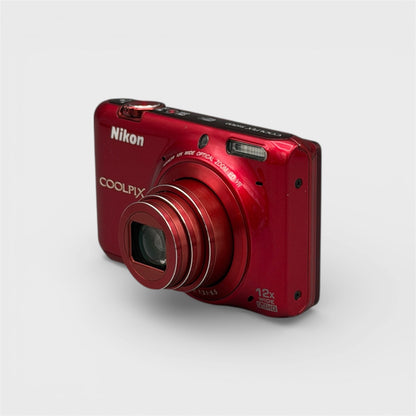 Red Nikon Coolpix S6500 viewed from a front angle showing its extended lens and side panel.