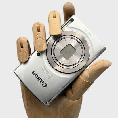 Silver Canon PowerShot ELPH 180 held in a wooden display hand with its lens closed.