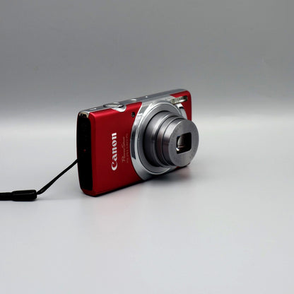 Angled front view of a red Canon PowerShot ELPH 140 IS showing its extended lens and black side panel