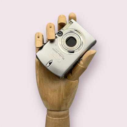 Silver Canon PowerShot SD550 held in a wooden display hand with its lens retracted.